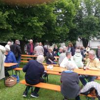Viele Besucher sitzen beim „Picknick für Alle“ 2024 an bereitgestellten Holztischen und Bänken.