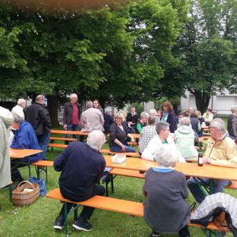 Viele Besucher sitzen beim „Picknick für Alle“ 2024 an bereitgestellten Holztischen und Bänken.