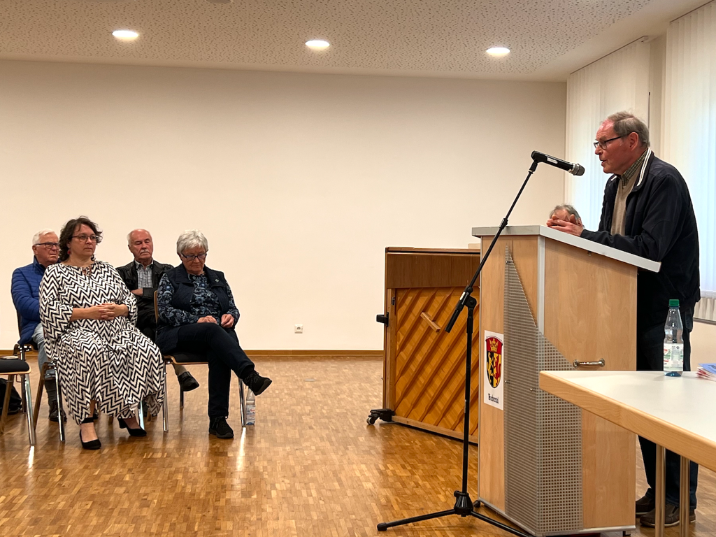 Nahaufnahme des Sprechers und zweier aufmerksamer Teilnehmer während der Gedenkfeier zum 8. Mai im Bürgerhaus Rodheim.