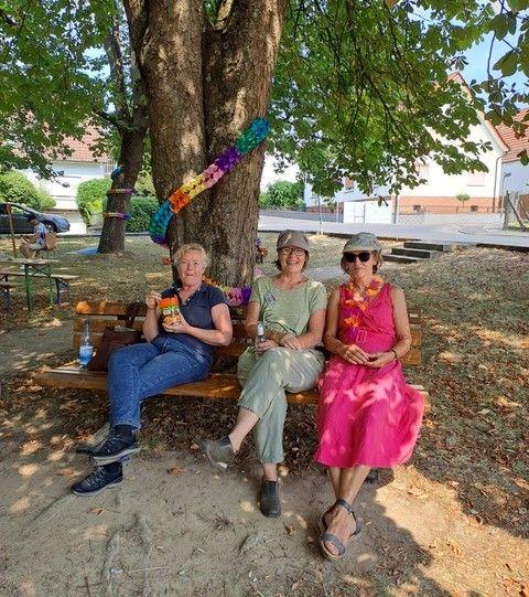 Drei Frauen sitzen im Schatten unter einem großen Baum.