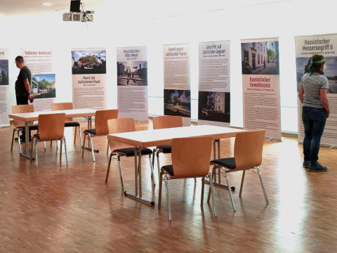 Blick in den hell beleuchteten Ausstellungsraum der Wanderausstellung mit Informationstafeln und vereinzelten Stühlen.